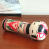 Cylindrical Creative Kokeshi doll by Miho Sasaki, featuring hand-painted chrysanthemums in red, green, and purple, with a rounded top and artist’s signature on the base. Buy online at j-okini.com in Malta