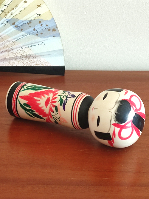 Cylindrical Creative Kokeshi doll by Miho Sasaki, featuring hand-painted chrysanthemums in red, green, and purple, with a rounded top and artist’s signature on the base. Buy online at j-okini.com in Malta