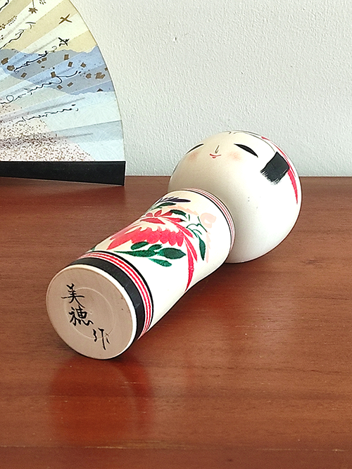 Cylindrical Creative Kokeshi doll by Miho Sasaki, featuring hand-painted chrysanthemums in red, green, and purple, with a rounded top and artist’s signature on the base. Buy online at j-okini.com in Malta