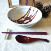 A beautifully curated Japanese ramen dining set featuring a handcrafted white ramen bowl with red accents, rose red wooden spoon, hexagonal chopsticks, and a ceramic chopstick rest, elegantly displayed on a white textured background. j-okini.com in Malta