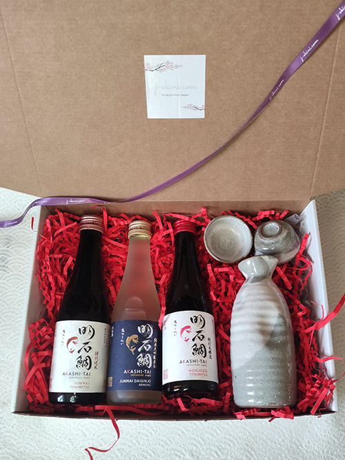 Premium sake gift box with Junmai Daiginjo, Junmai Tokubetsu, Honjozo Tokubetsu, and a Mino-ware sake set in rustic white and gray tones. Available at j-okini.com in Malta