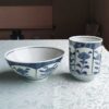 Banko-yaki Yunomi tea cup and rice bowl set featuring alternating floral motifs framed in rectangular panels, with delicate blue indigo hues, crafted by the Aigama kiln in Yokkaichi, Japan. Available at j-okini.com in Malta.