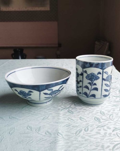 Banko-yaki Yunomi tea cup and rice bowl set featuring alternating floral motifs framed in rectangular panels, with delicate blue indigo hues, crafted by the Aigama kiln in Yokkaichi, Japan. Available at j-okini.com in Malta.