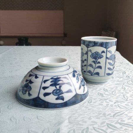 Banko-yaki Yunomi tea cup and rice bowl set featuring alternating floral motifs framed in rectangular panels, with delicate blue indigo hues, crafted by the Aigama kiln in Yokkaichi, Japan. Available at j-okini.com in Malta.