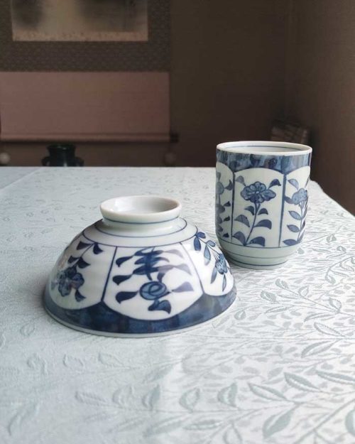 Banko-yaki Yunomi tea cup and rice bowl set featuring alternating floral motifs framed in rectangular panels, with delicate blue indigo hues, crafted by the Aigama kiln in Yokkaichi, Japan. Available at j-okini.com in Malta.