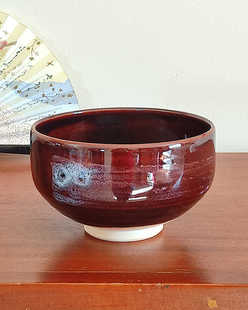 A handmade Kiyomizu-ware Matcha bowl by Okayama Kousha, featuring a deep amber glaze with vibrant blue accents, a low tube shape, and a wide opening for easy use. available at j-okini.com in malta