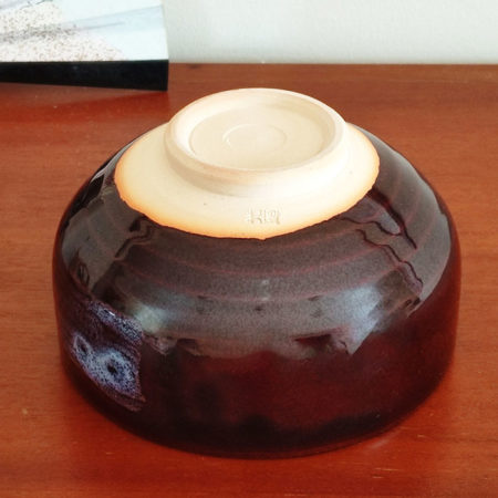 A handmade Kiyomizu-ware Matcha bowl by Okayama Kousha, featuring a deep amber glaze with vibrant blue accents, a low tube shape, and a wide opening for easy use. available at j-okini.com in malta