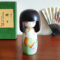 Handcrafted Japanese Kokeshi doll 'Chouchou' by artist Fujikawa Shoei, featuring a light green Michiyuki kimono jacket with a butterfly and pink floral design. Available at j-okini.com in Malta