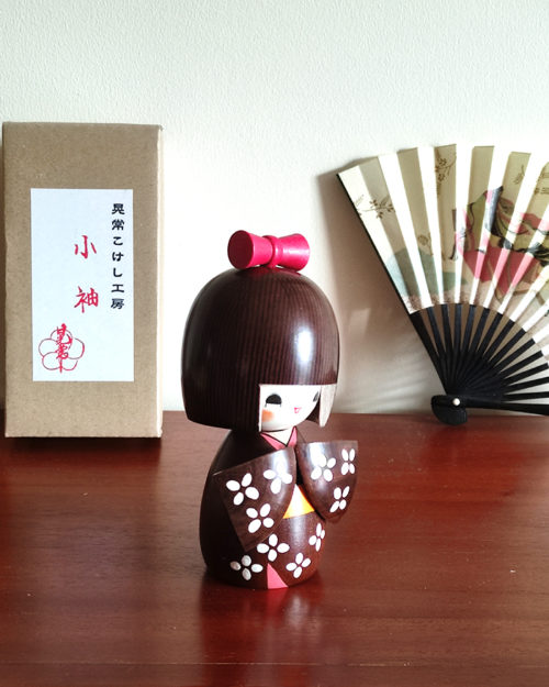 Handcrafted Japanese Kokeshi doll 'Kosode' by artist Kojo, wearing a chic brown kimono with a soft pink collar and a vibrant yellow obi. Available at j-okini.com in Malta