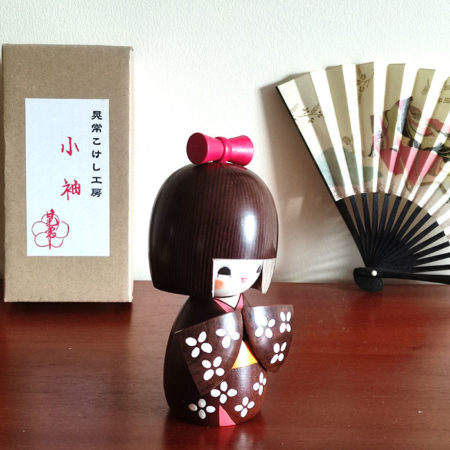 Handcrafted Japanese Kokeshi doll 'Kosode' by artist Kojo, wearing a chic brown kimono with a soft pink collar and a vibrant yellow obi. Available at j-okini.com in Malta