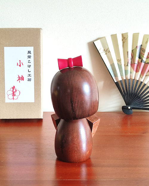 Handcrafted Japanese Kokeshi doll 'Kosode' by artist Kojo, wearing a chic brown kimono with a soft pink collar and a vibrant yellow obi. Available at j-okini.com in Malta