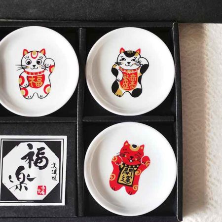 A set of five Japanese Maneki-Neko small dishes, each featuring a unique beckoning cat design symbolizing luck, protection, happiness, prosperity, and wealth. Perfect for serving soy sauce or condiments. Made in Japan. Available at j-okini.com in Malta