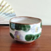 Mino ware Matcha bowl featuring a purple Camellia design with green leaves, a winding dark green-brown rim, and a swirl pattern inside. Made in Japan. Available at j-okini.com in Malta