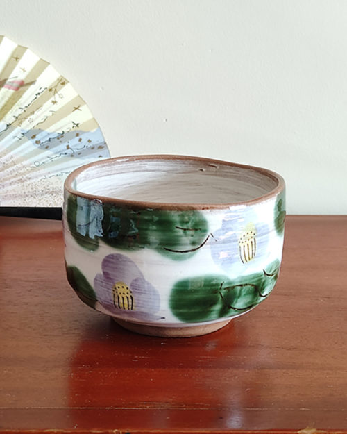 Mino ware Matcha bowl featuring a purple Camellia design with green leaves, a winding dark green-brown rim, and a swirl pattern inside. Made in Japan. Available at j-okini.com in Malta