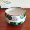 Mino ware Matcha bowl featuring a purple Camellia design with green leaves, a winding dark green-brown rim, and a swirl pattern inside. Made in Japan. Available at j-okini.com in Malta