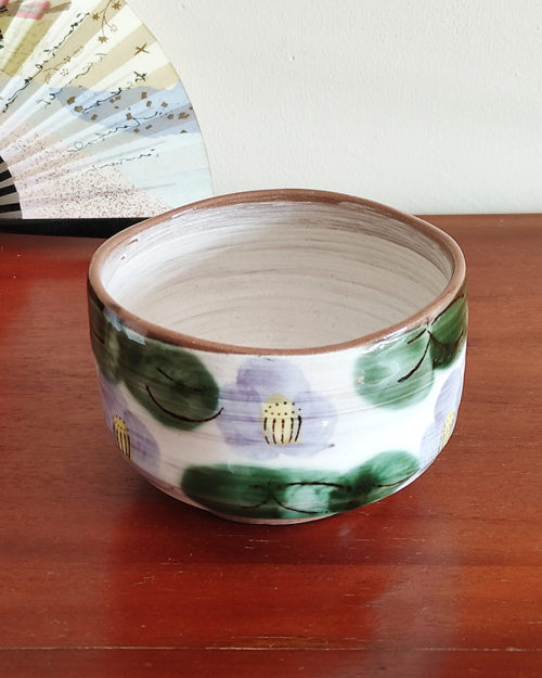 Mino ware Matcha bowl featuring a purple Camellia design with green leaves, a winding dark green-brown rim, and a swirl pattern inside. Made in Japan. Available at j-okini.com in Malta