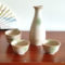 A glazed Kiseto Sake Set with a beige tokkuri bottle and matching sake cups, each featuring soft green accents and a smooth, speckled finish. Made in Japan. Available at j-okini.com in Malta