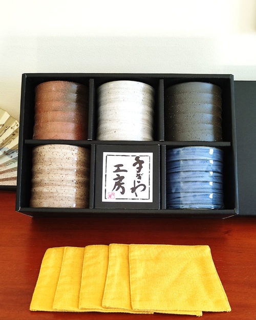 A set of five Kezuri Rock Glasses in earthy tones with mustard fabric coasters, elegantly packaged in a black gift box. Available at j-okini.com in Malta