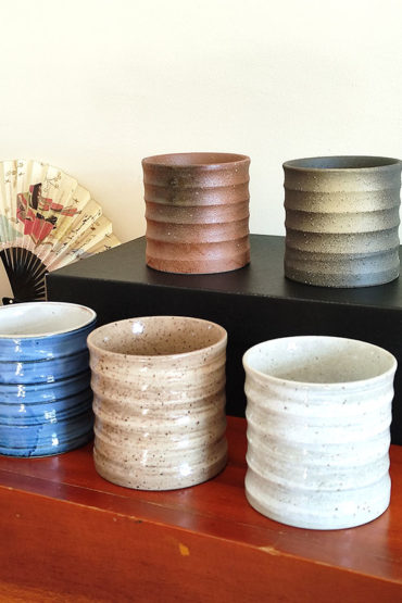 A set of five Kezuri Rock Glasses in earthy tones with mustard fabric coasters, elegantly packaged in a black gift box. Available at j-okini.com in Malta